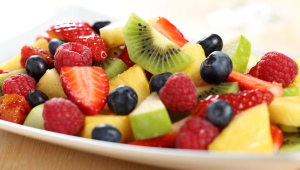 A plate filled with sliced and diced kiwis, apples, and various berries.