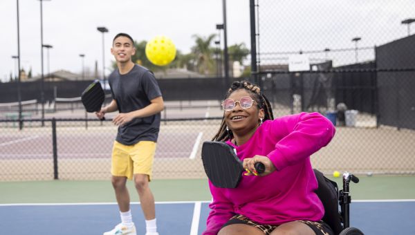 Young disabled Black person in a wheelchair playing pickleball with a friend