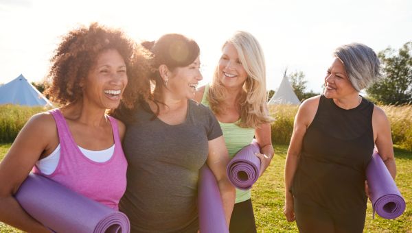 Group of four young and middle aged women with their arms around each other, while smiling and holding yoga mats