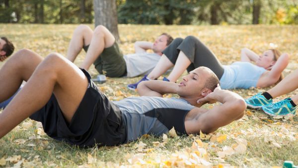 Young man doing crunches in a group exercise class outdoors