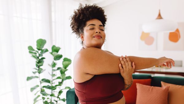 Young woman smiling and stretching her arms in the living room during an at-home workout.