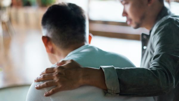 son consoling his father with a hand on his back