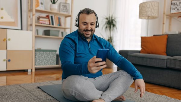 a happy middle aged white man with a beard sits on a yoga mat looking at his smartphone