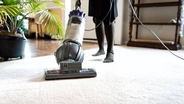 closeup of a woman's feet using a vacuum cleaner to clean a carpet in a home