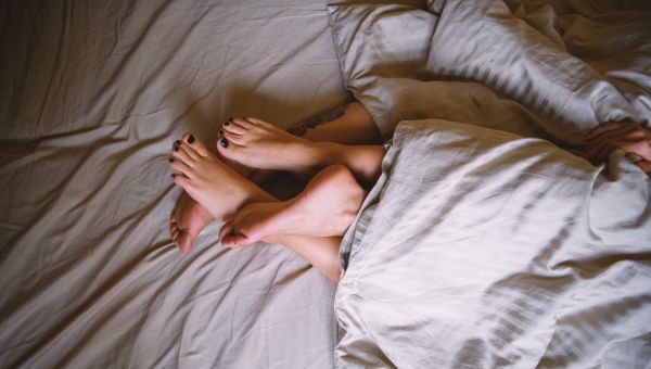 a pair of feet stick out from under sheets on a bed