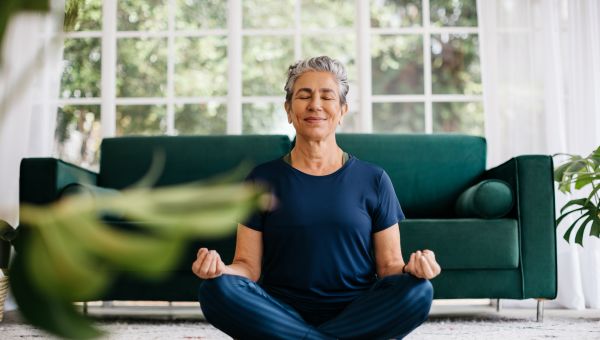 a middle aged Latina woman with short gray hair sits smiling and meditating in a yoga pose