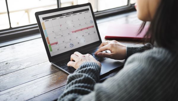 an Asian woman sits a computer and adds important information to her online calendar