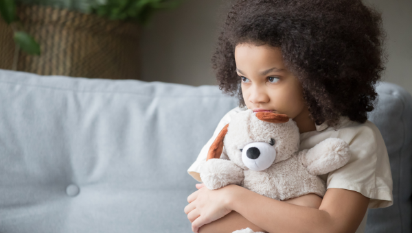 young girl sitting on couch at home squeezing a teddy bear anxious about home life