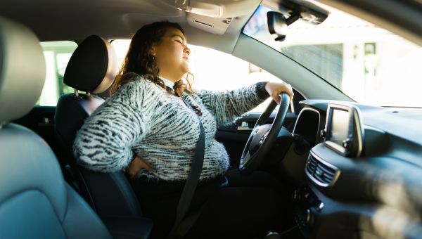side view of a young woman in a car, reaching for her back in pain