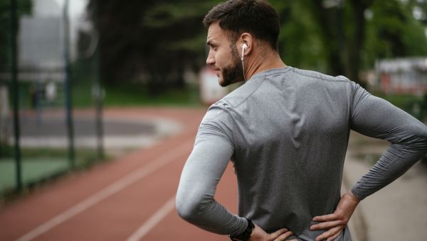 man standing on a running track holding his painful back