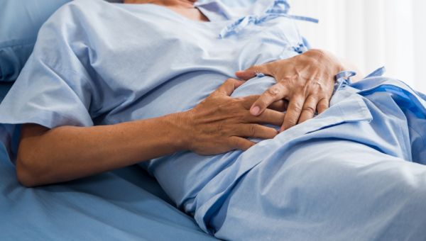 man in hospital bed after surgery holding his abdomen in pain