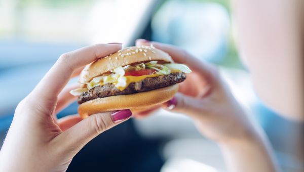 woman's hands holding a fast food hamburger in her car