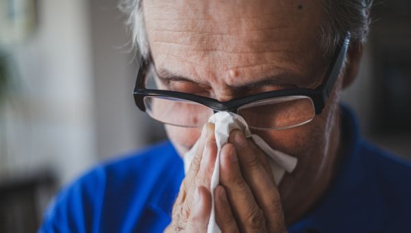 senior man with allergies blowing his nose into a tissue