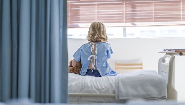 rear view of child with teddy bear on hospital bed