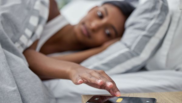 woman in bed reaching for phone