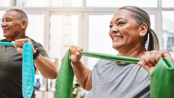 a Latina woman uses a resistance band to strengthen her shoulder and chest muscles