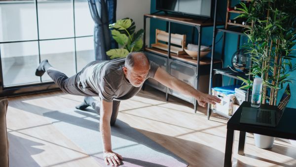 an older white man does plank exercises on the floor of his home using a computer as a guide on a cold winter's day