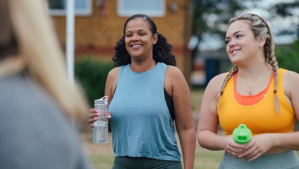 two young women are arriving together for an exercise class both holding water bottles