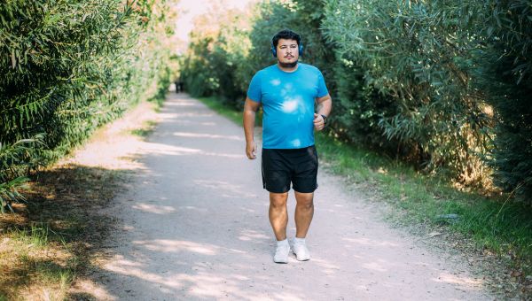 an overweight young man is outside walking on a path in the woods
