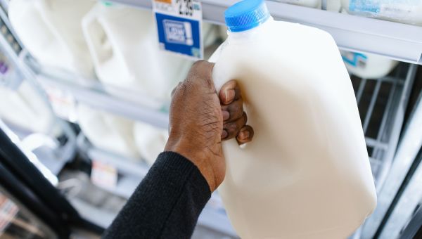 closeup image of a woman's hand holding a carton of milk at the grocery store