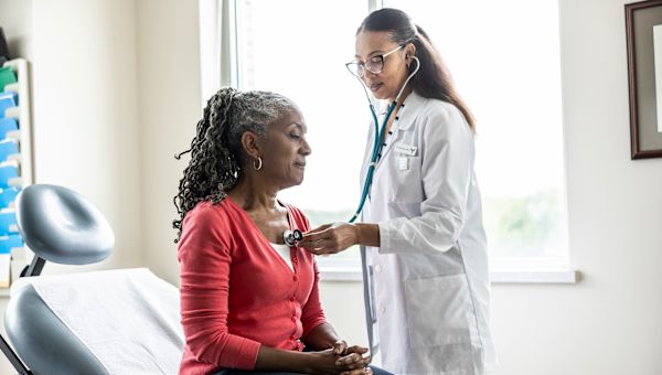 doctor listens to female patient's heart with stethoscope