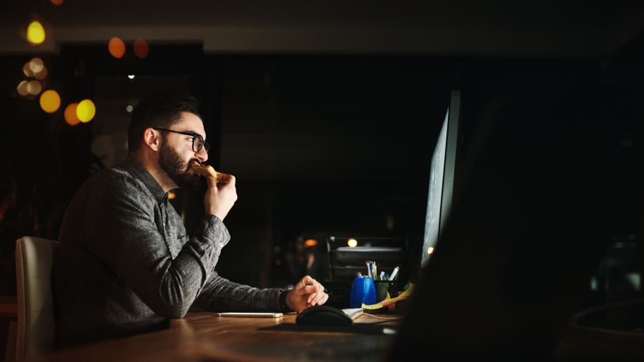 Man in glasses at night on computer eating