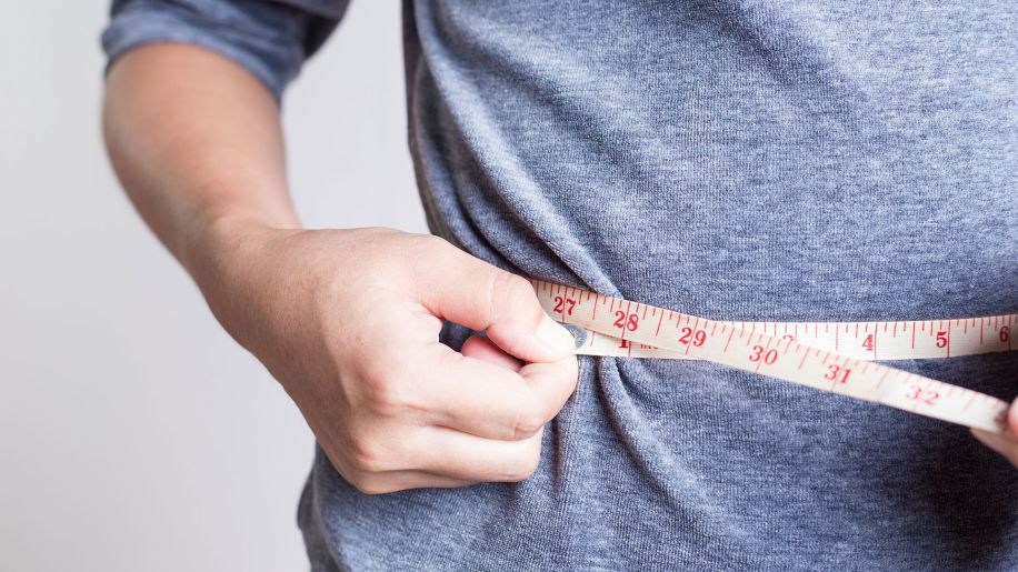 Man measures his waist side with a measuring tape.