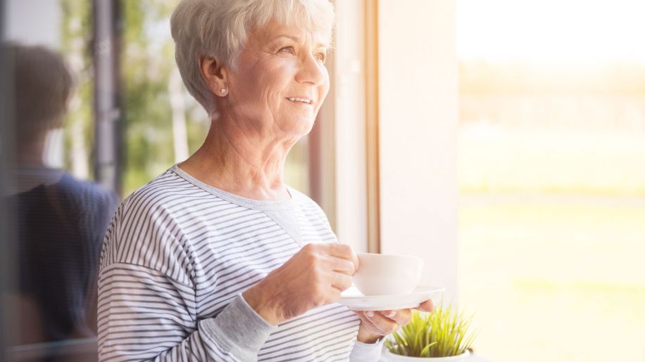 Elderly woman drinking tea outside.