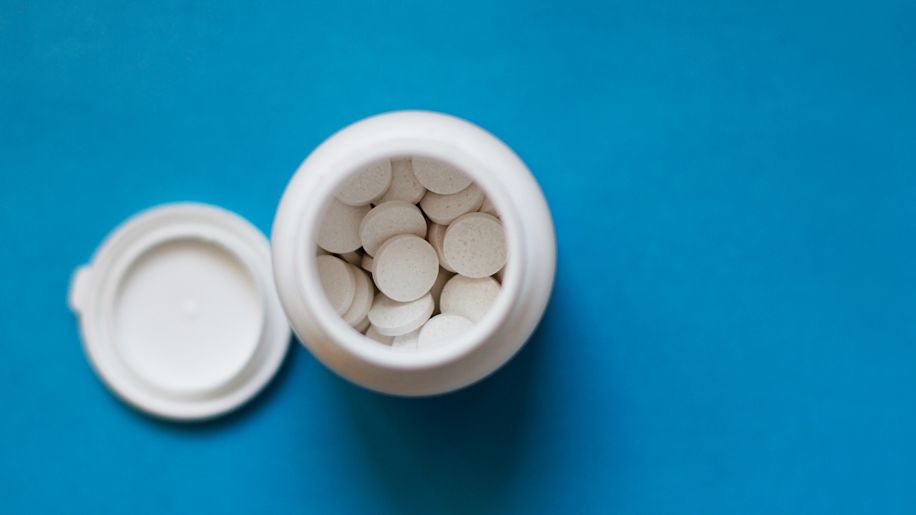 White pill bottle with pills inside on blue background.
