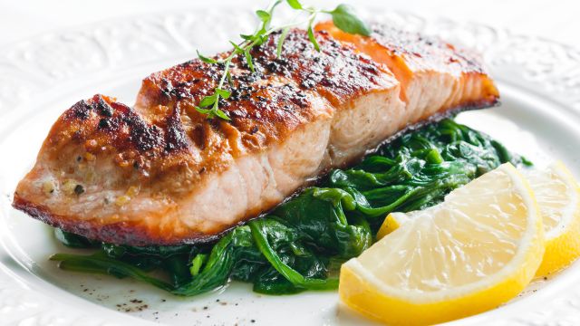salmon fillet, sauteed spinach, and lemon slices on a white place