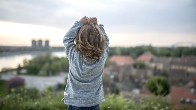 Rear view of little boy standing outdoors with hands on head and admiring the view.