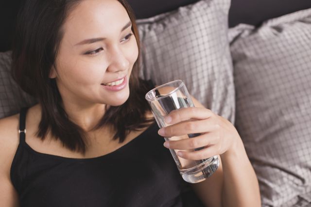 Women drinking water on the bed. Her smiling.