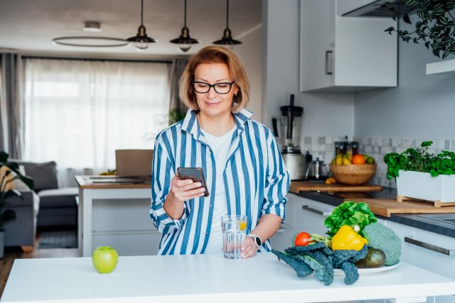 Happy woman standing at the open refrigerator with fruits, vegetables and healthy food