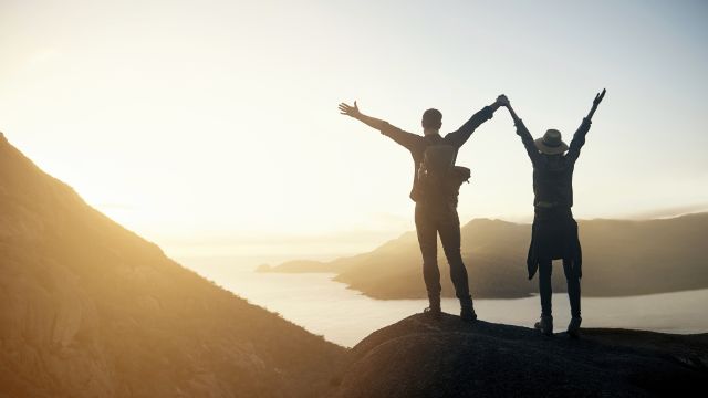 Couple standing on a rock with their hands in the air