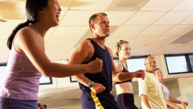 Side profile of five people doing step aerobics in a gym