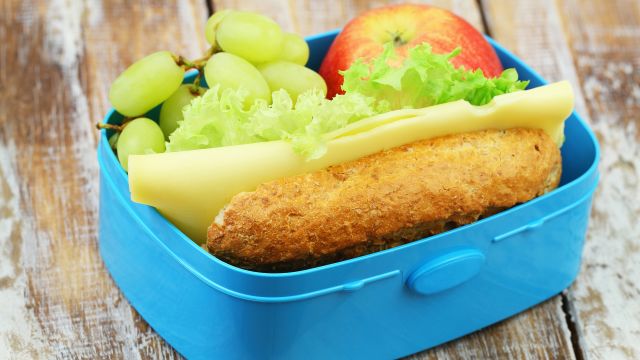 Healthy lunch box containing brown bread roll with cheese and lettuce, red apple and grapes