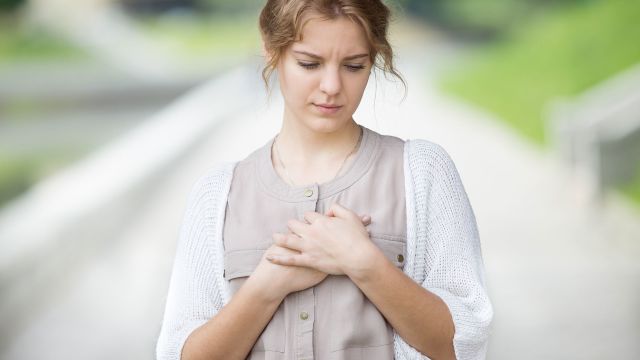woman holding chest, hands on chest, heart palpitation