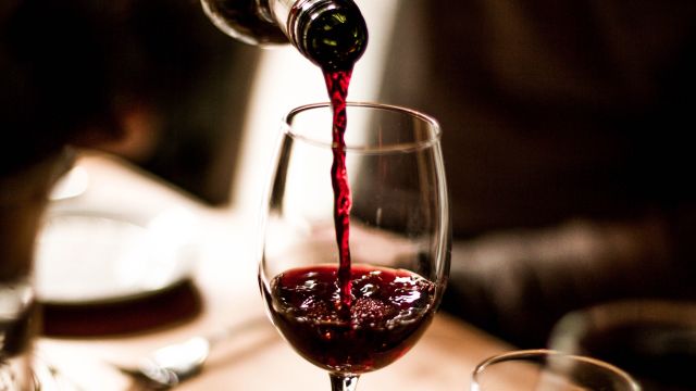 Someone pours a small amount of red wine into a glass—being careful not to pour too much wine.