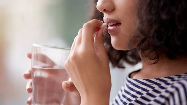 Young woman taking vitamin supplement with water