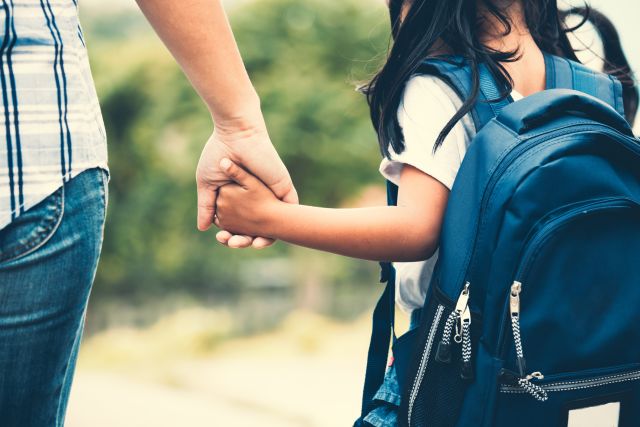 little girl wearing backpack holding hands