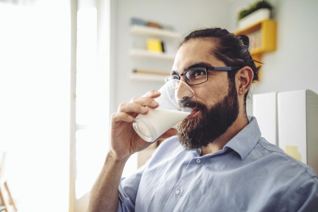 A man drinks a large glass of milk to get his daily calcium intake and recommended dose of vitamin D.
