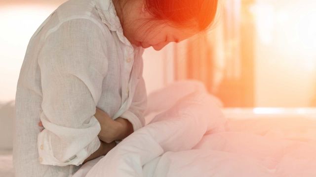 A woman sits in bed clutching her stomach, suffering from one of the many different types of IBS (irritable bowel syndrome).