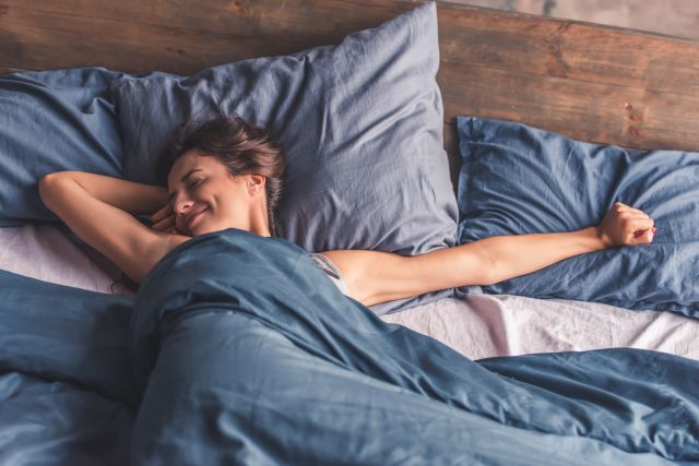 Young woman in blue bed stretching waking up from sleep