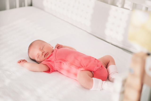 Newborn baby in pink outfit asleep in crib