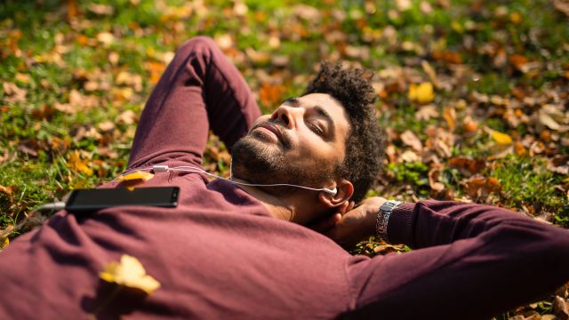 Practicing lifestyle changes for ulcerative colitis, a man reduces his stress by relaxing on leaves listening to music.