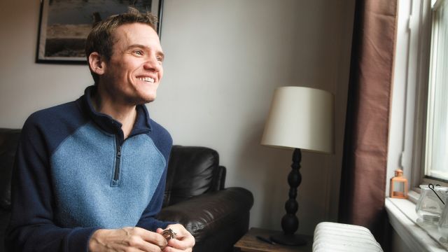 Transgender man looking out the window with a smile on his face.