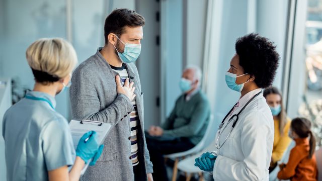 Young man holding his chest talking to a doctor about his symptoms.