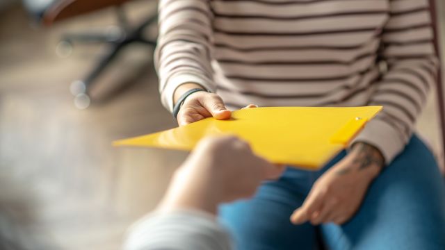 A physician hands a patient a folder containing medical records.