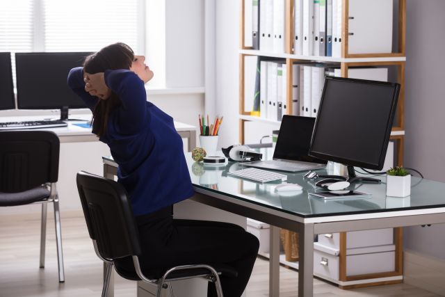 Smiling woman sits in office chair doing an exercise with elbows extended.