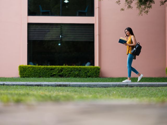 a young woman walks on a college campus against the background of a pink building